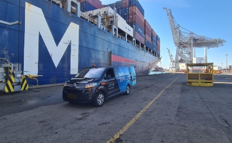 Camion utilitaire devant un grand porte-conteneurs dans un port industriel en activité