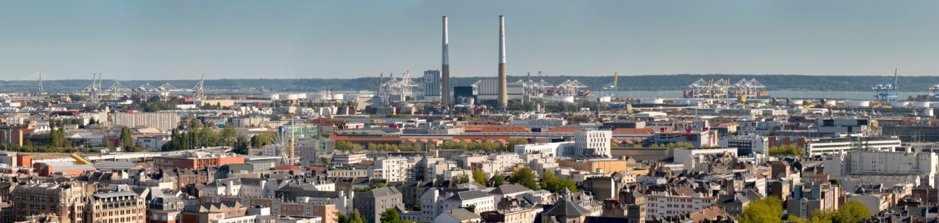 Vue panoramique d’une ville portuaire avec zone urbaine dense, port industriel et grues au bord de la mer