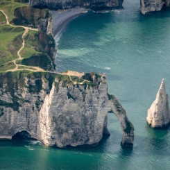 Vue aérienne de falaises blanches avec arche naturelle et aiguille rocheuse dominant une mer turquoise