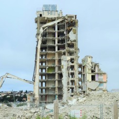 Démolition d’un immeuble en béton partiellement effondré avec pelle mécanique sur un chantier rempli de gravats