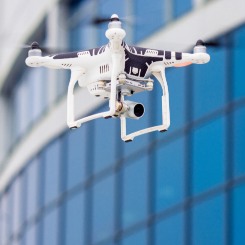 Drone blanc en vol avec caméra stabilisée devant un bâtiment moderne aux vitres bleutées